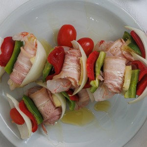 Brochettes de langostinos envueltos en panceta, cebolla morada, morrones y ananá fresca